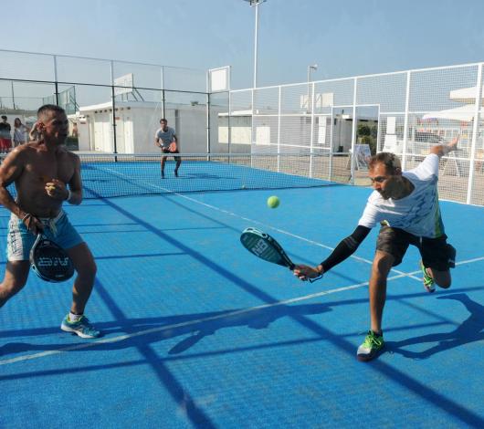 Giocatori di padel in azione su un campo blu all'aperto.