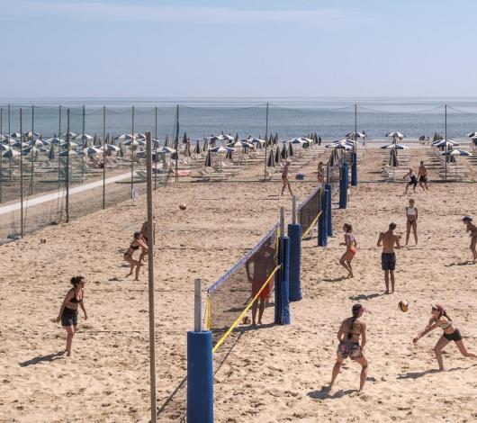 Persone giocano a beach volley su una spiaggia con ombrelloni.