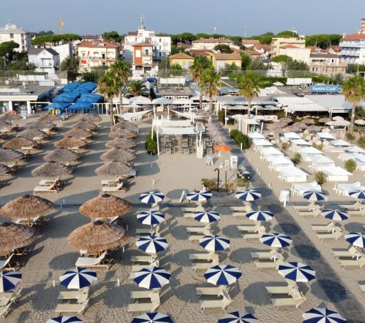 Spiaggia con ombrelloni e lettini, edifici sullo sfondo.