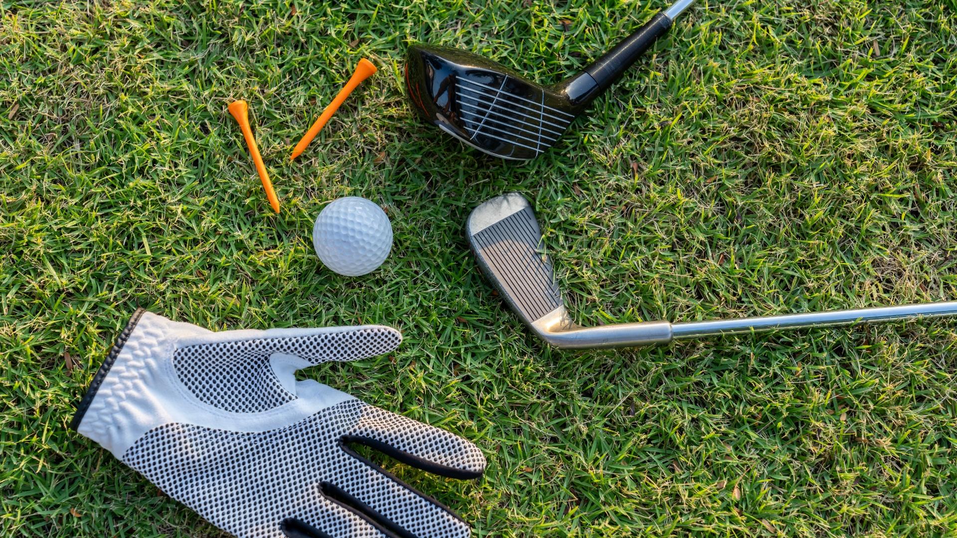 Attrezzatura da golf su erba: mazze, guanti, pallina e tee arancioni.