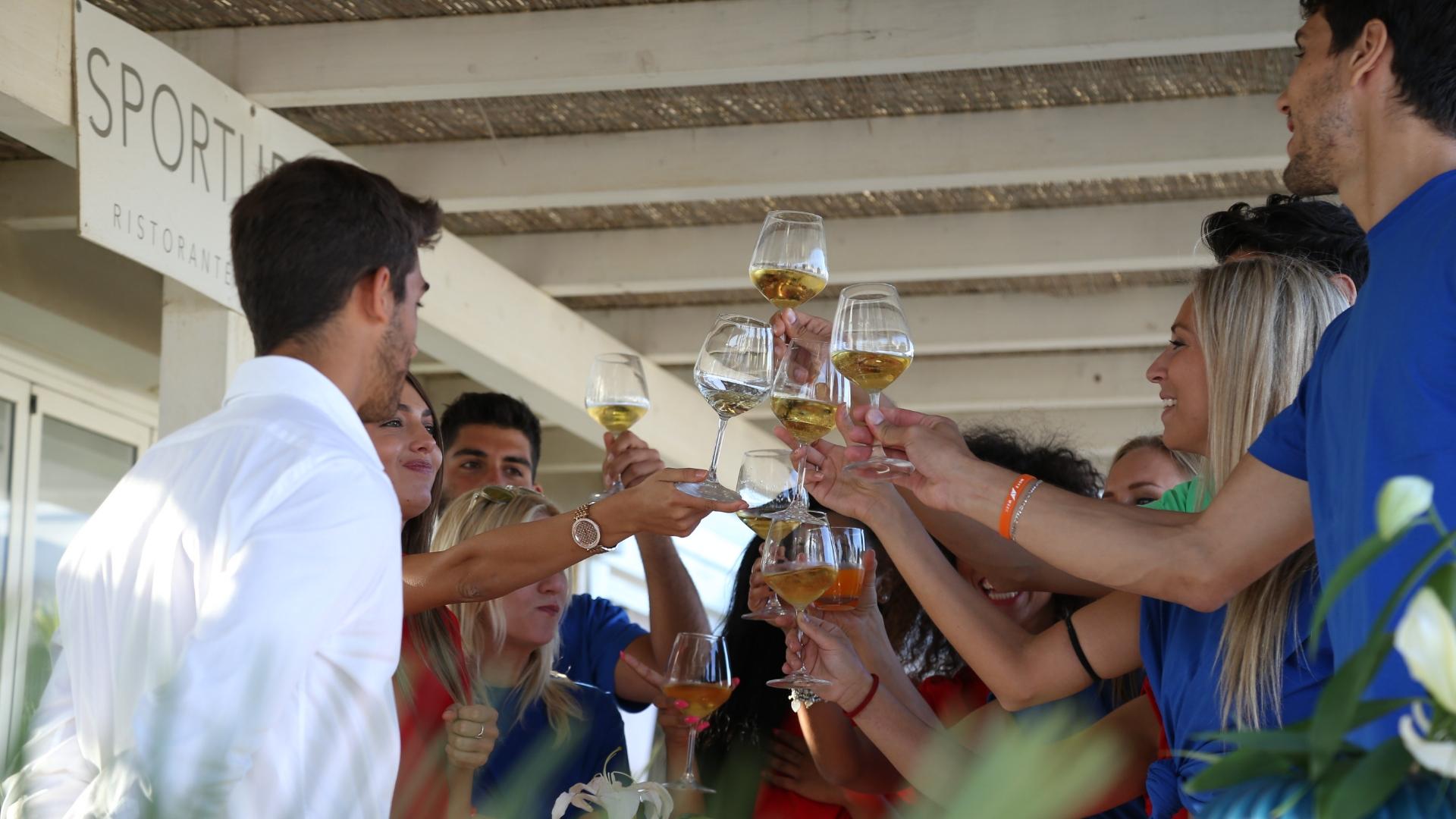 Persone brindano con bicchieri di vino bianco in un ristorante all'aperto.