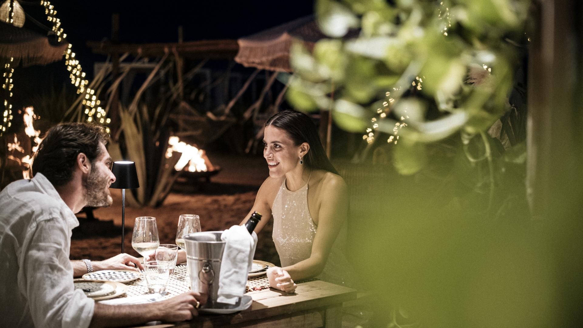 Cena romantica in spiaggia con luci soffuse e atmosfera intima.