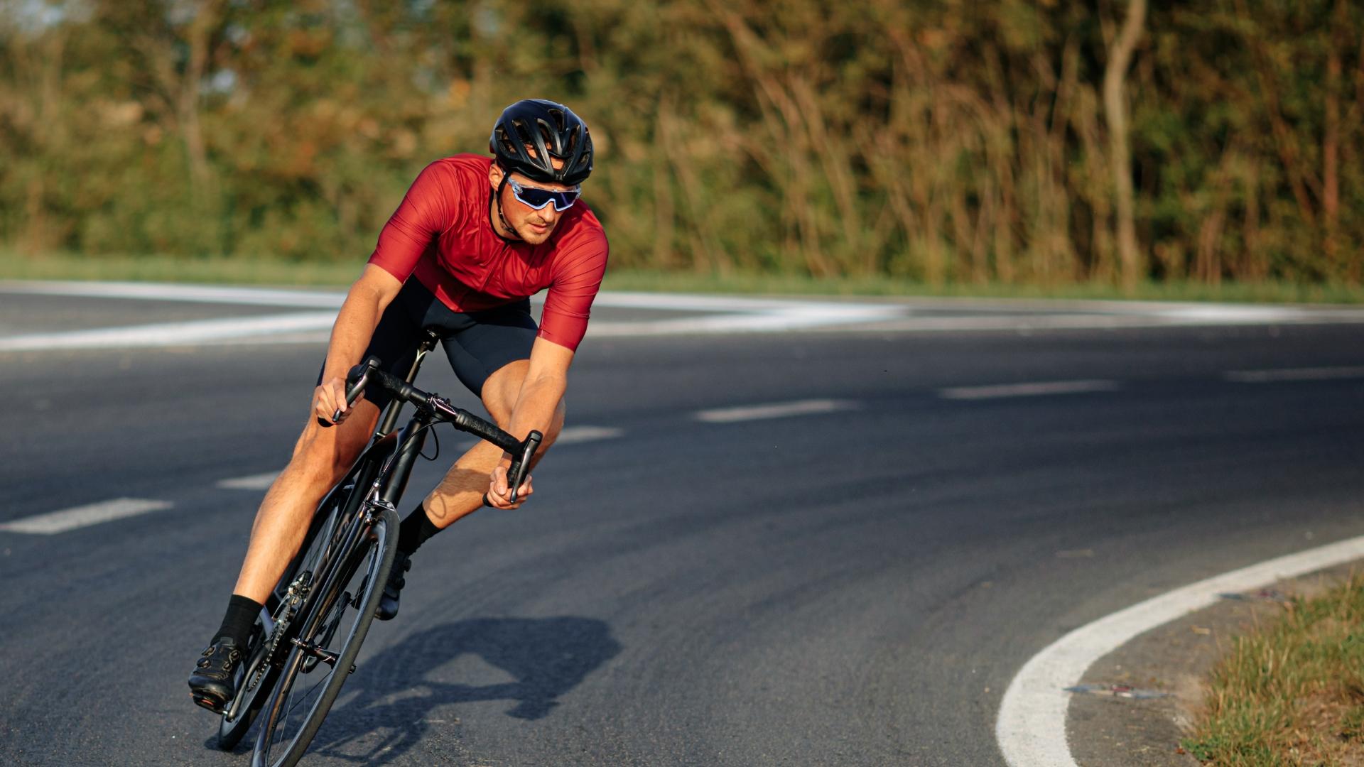 Ciclista in curva su strada asfaltata, indossa casco e occhiali da sole.