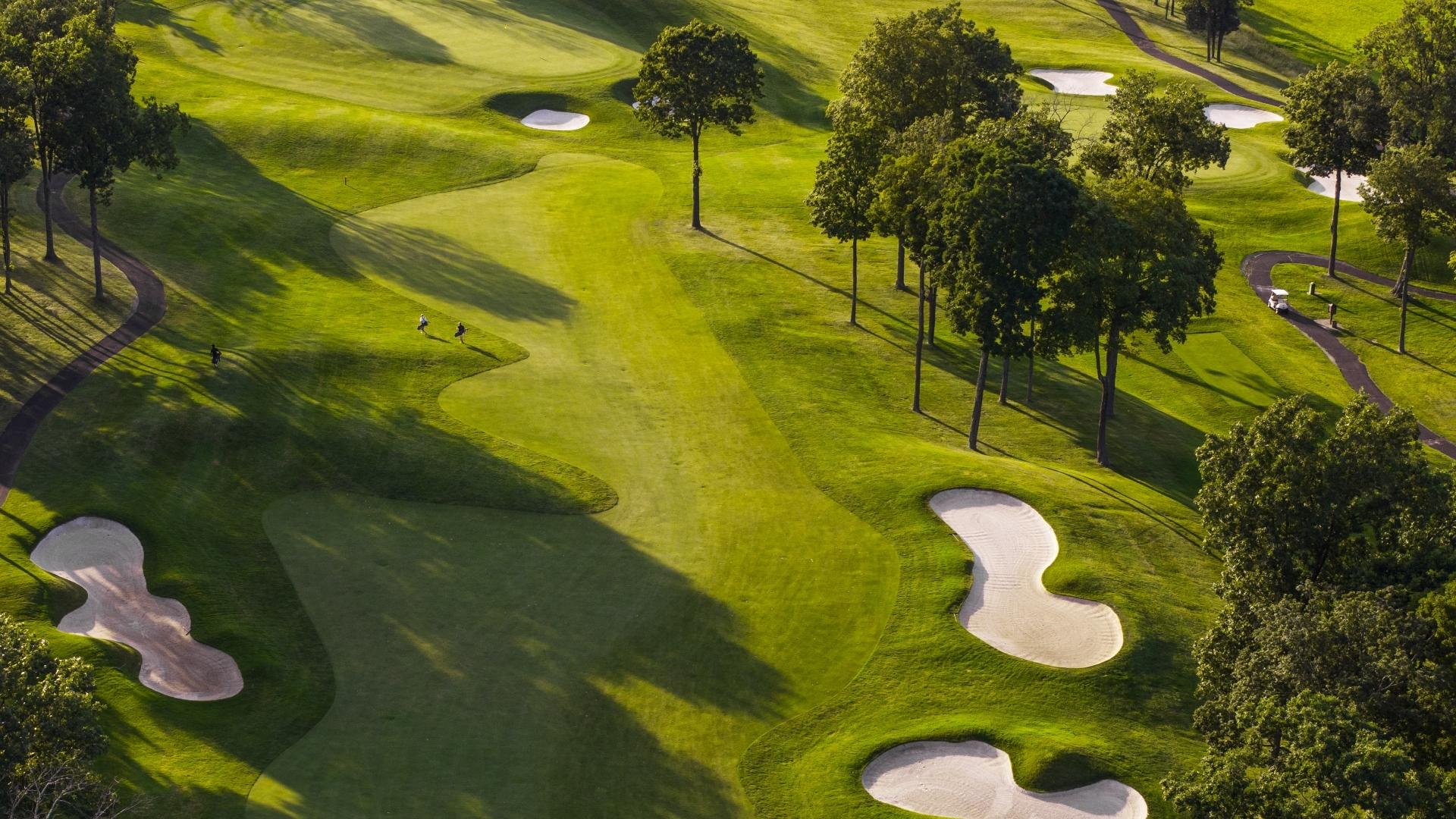 Campo da golf con green, bunker e alberi, visto dall'alto.