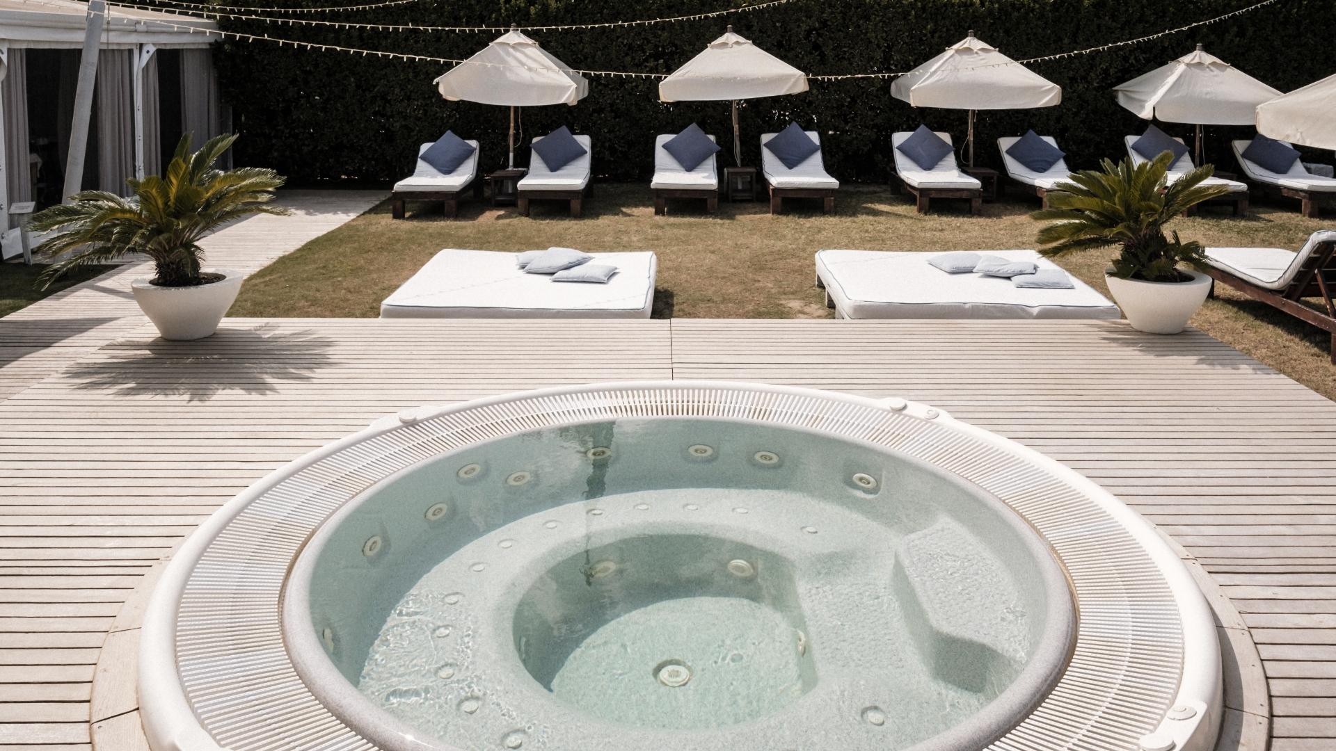 Piscina con idromassaggio, lettini e ombrelloni in un'area relax all'aperto.