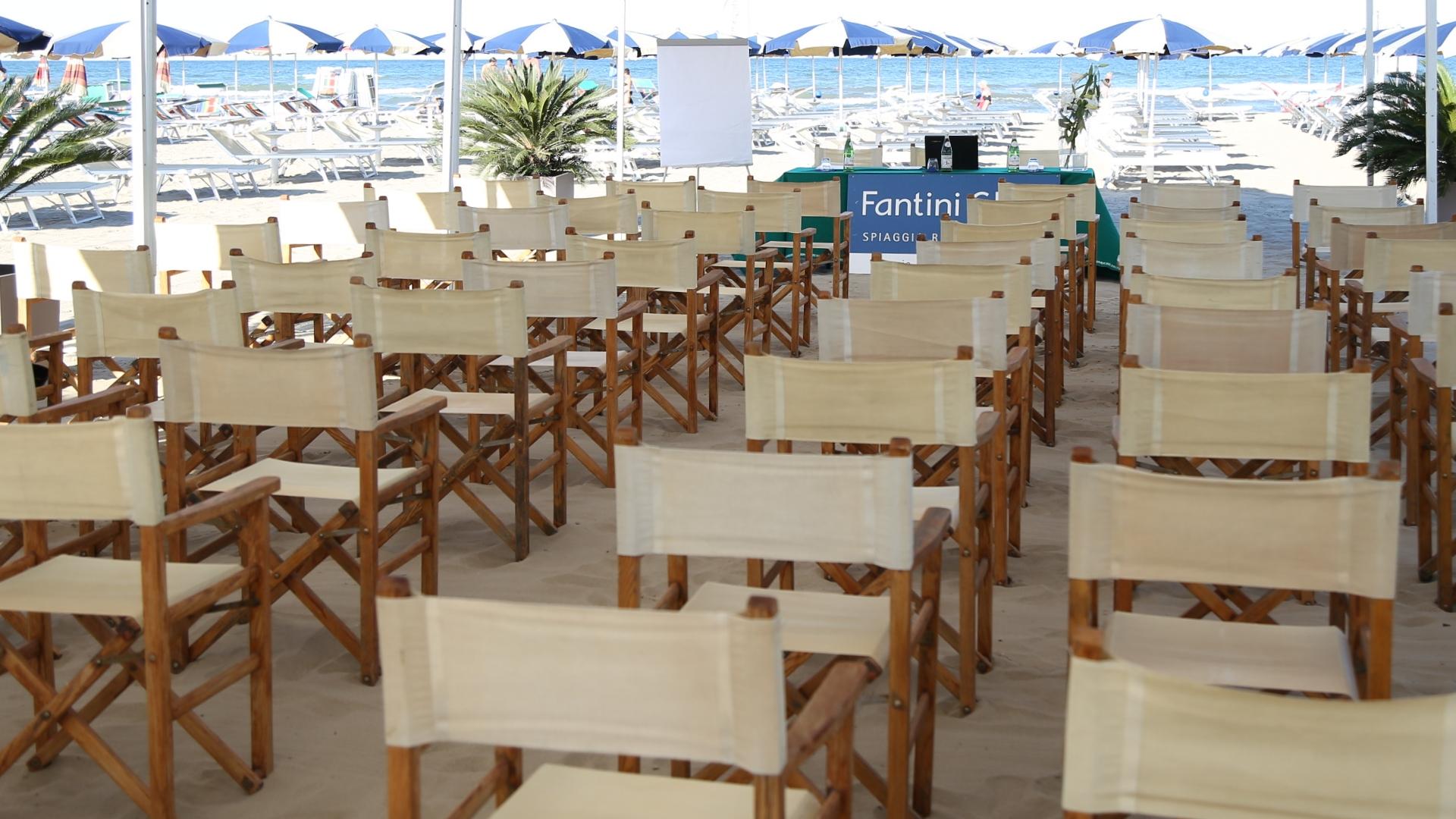 Sedie disposte su una spiaggia, con ombrelloni e mare sullo sfondo.