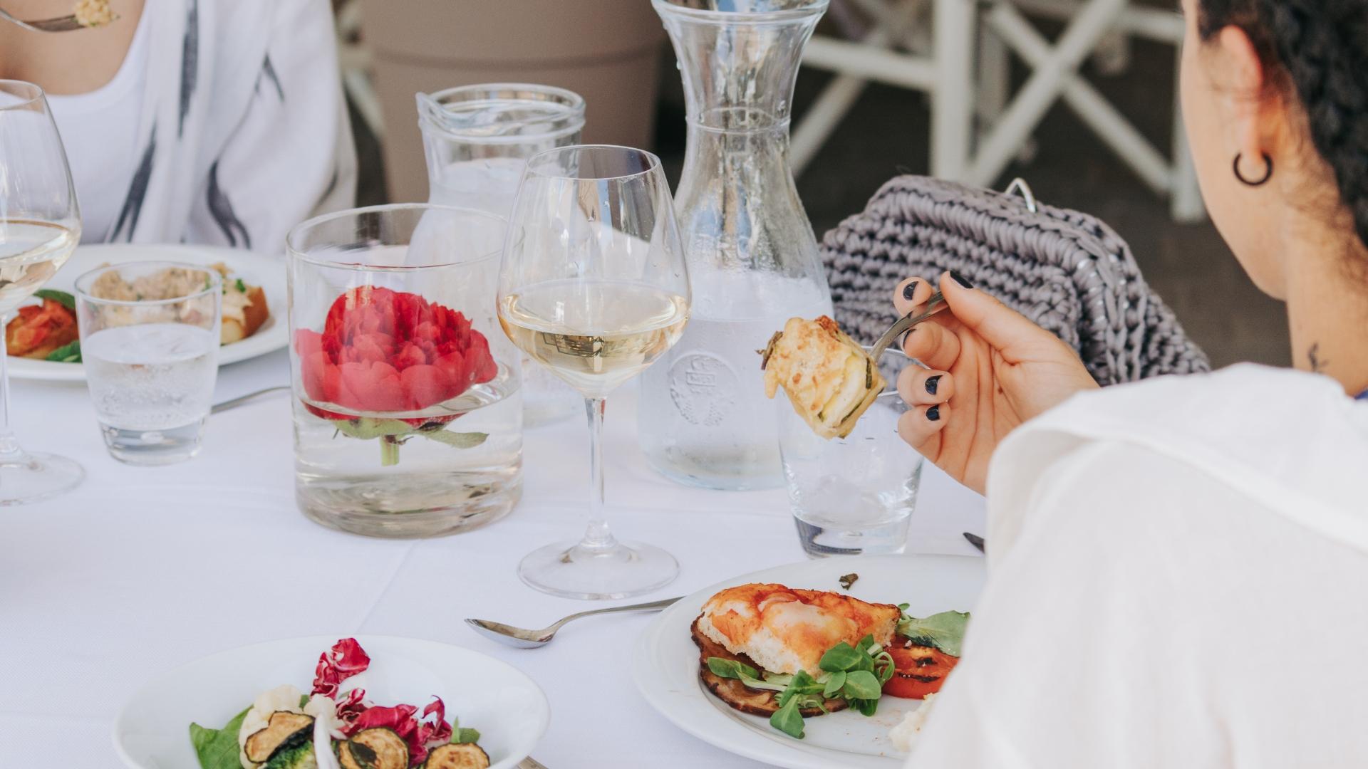 Pranzo elegante con vino bianco, fiori e piatti raffinati su tavola apparecchiata.