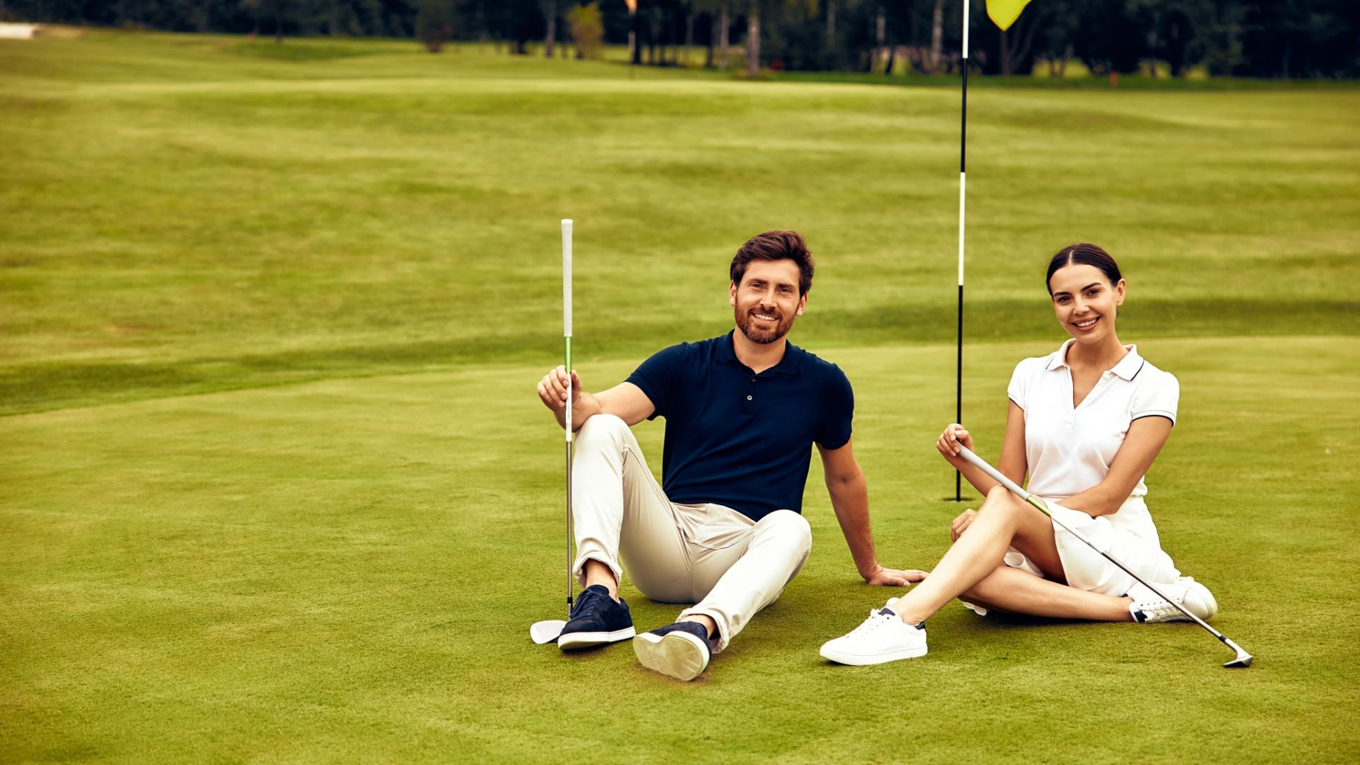 Coppia seduta su un campo da golf, sorridente con mazze da golf.