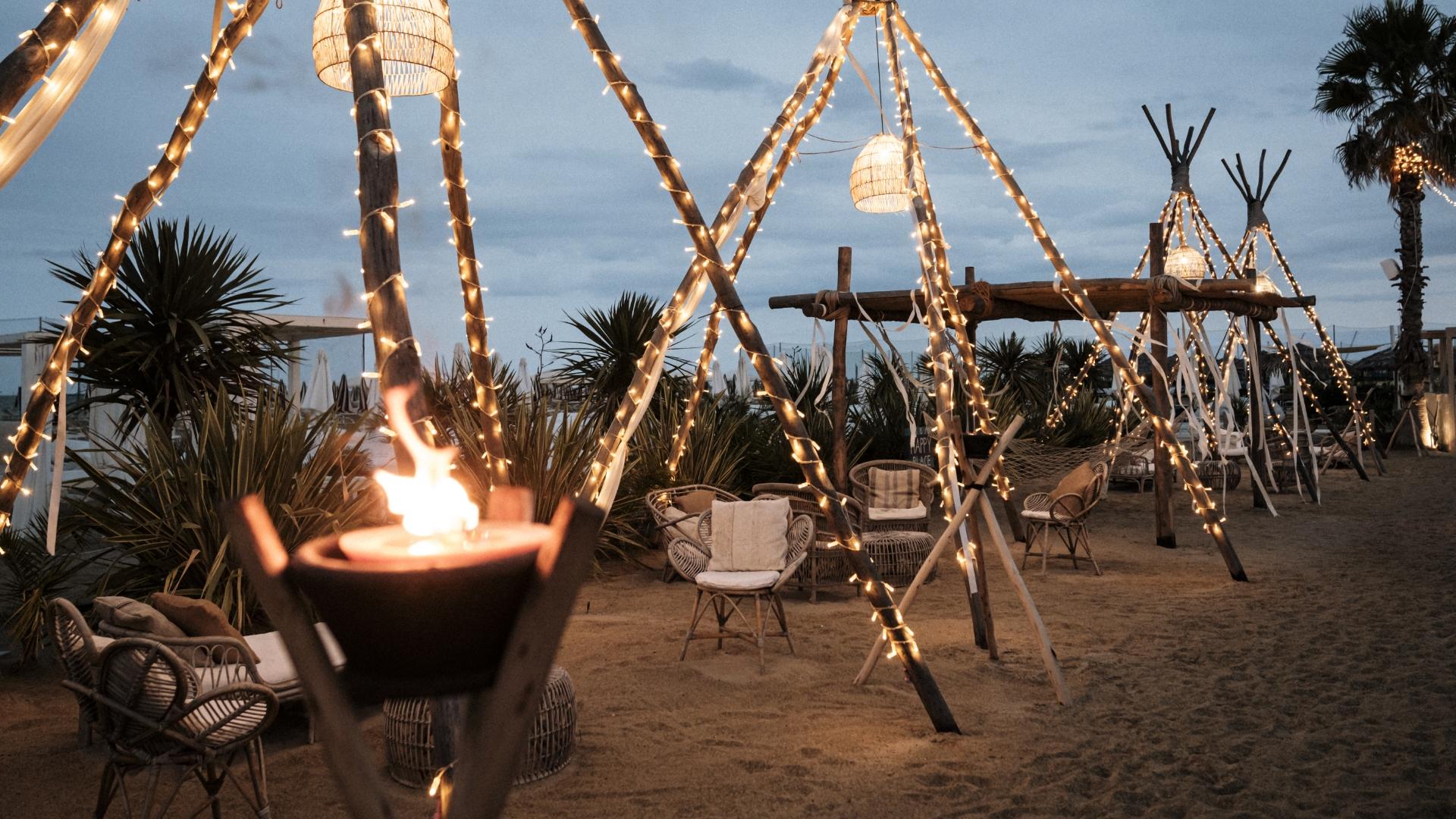 Spiaggia con luci decorative e sedie in vimini, atmosfera accogliente e rilassante.