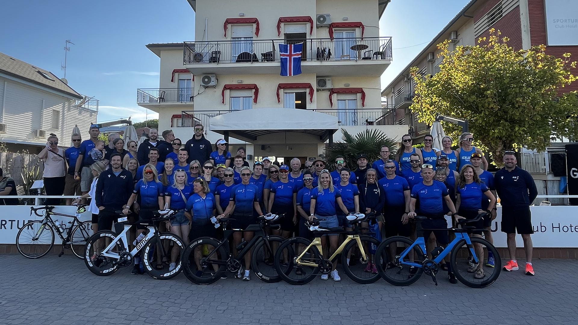 Gruppo di ciclisti in maglia blu davanti a un edificio con bandiera islandese.