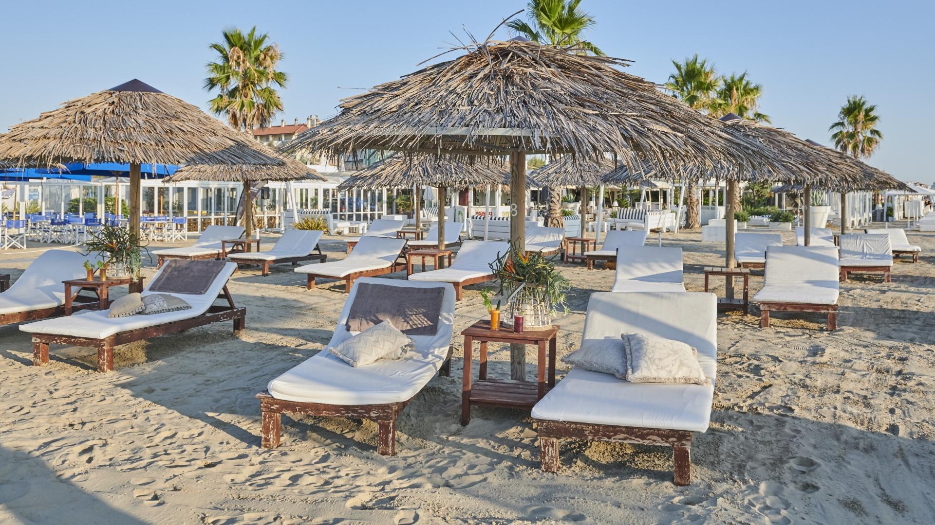 Spiaggia con lettini bianchi, ombrelloni di paglia e palme, atmosfera rilassante.