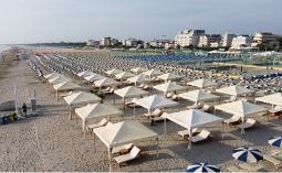 Spiaggia con ombrelloni e lettini, vista su edifici sul lungomare.