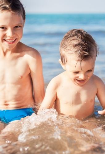 Due bambini giocano felici in acqua al mare, sorridendo e schizzando.