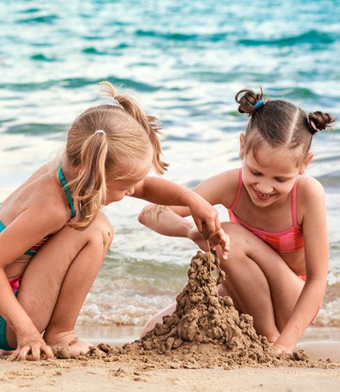 Due bambine costruiscono un castello di sabbia sulla spiaggia vicino al mare.