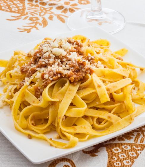 Tagliatelle al ragù con formaggio grattugiato su piatto quadrato bianco.