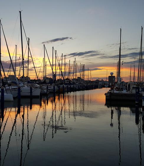 Tramonto su una marina con barche a vela riflette nell'acqua calma.