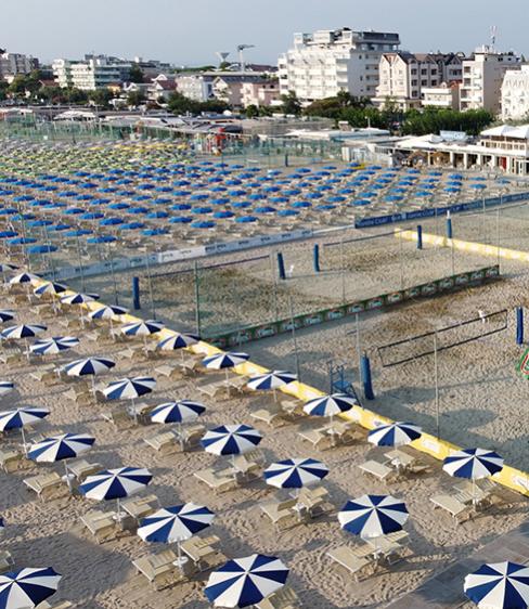 Spiaggia attrezzata con ombrelloni, lettini e campi da beach volley, vista dall'alto.