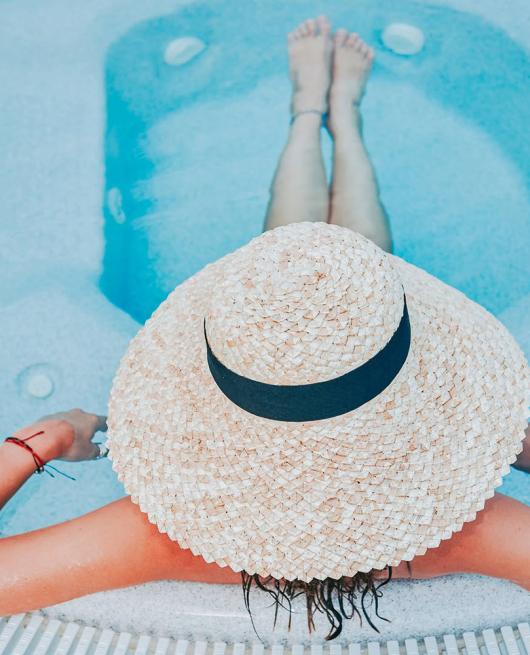 Persona rilassata in piscina con cappello di paglia, vista dall'alto.