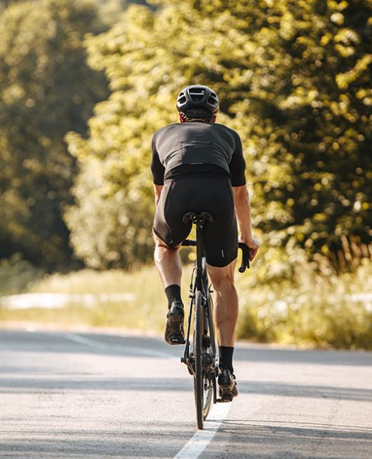 Ciclista in abbigliamento nero pedala su strada immersa nella natura.