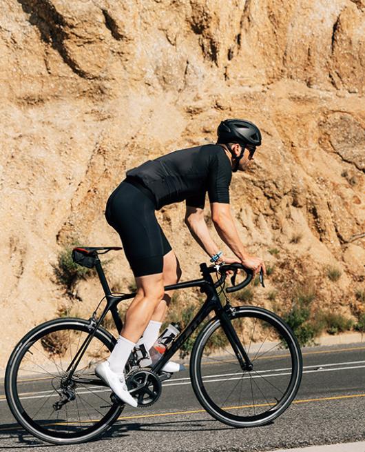 Ciclista in abbigliamento nero pedala su strada vicino a roccia.