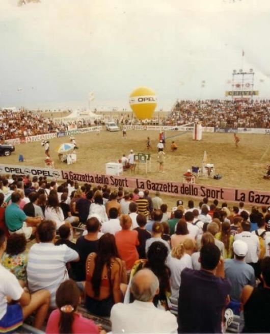 Partita di beach volley con pubblico numeroso, sponsorizzata da La Gazzetta dello Sport.