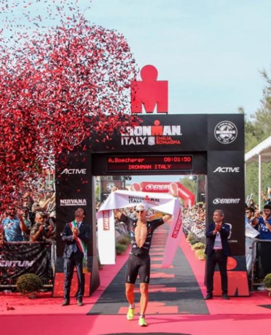 Vincitore dell'Ironman Italy Emilia-Romagna attraversa il traguardo tra applausi e coriandoli rossi.