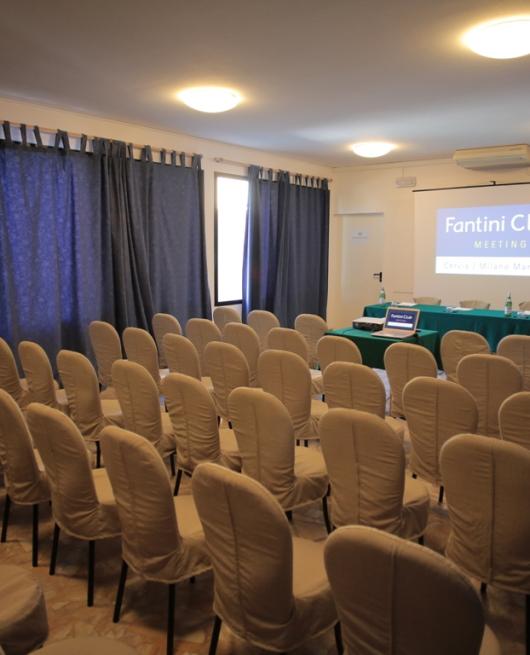 Sala conferenze con sedie coperte, proiettore e lavagna a fogli mobili.