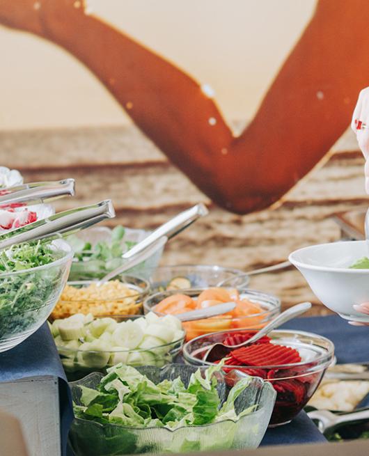 Persona prepara un'insalata al buffet con varie verdure fresche.