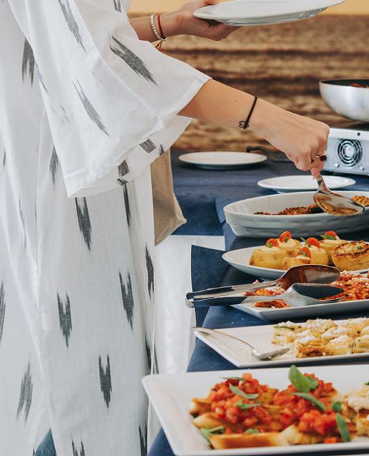 Buffet con piatti vari e persona che serve cibo su un piatto.