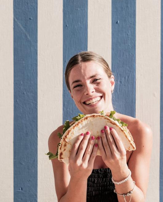 Donna sorridente con piadina davanti a parete a righe blu e bianche.