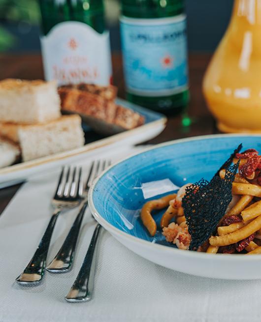 Piatto di pasta con pomodori secchi, pane e bicchiere di vino bianco.