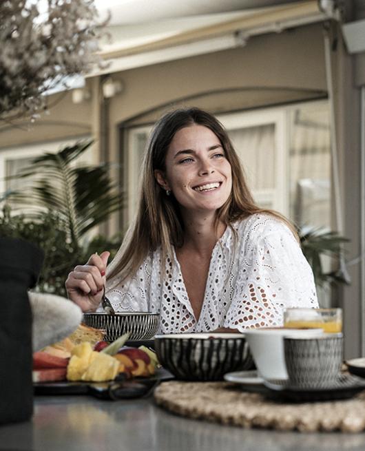 Due donne sorridenti condividono una colazione con frutta e pancake su un terrazzo.