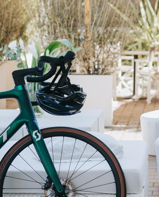 Bicicletta verde con casco appeso al manubrio, ambientata in un patio soleggiato.