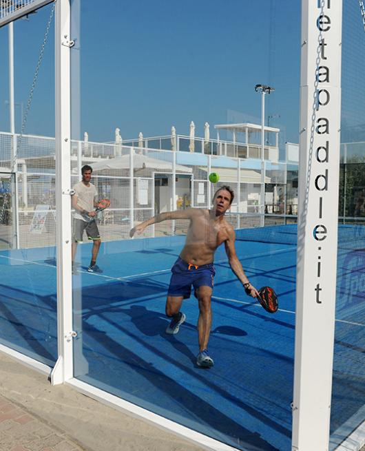 Due persone giocano a padel in un campo all'aperto con pavimento blu.