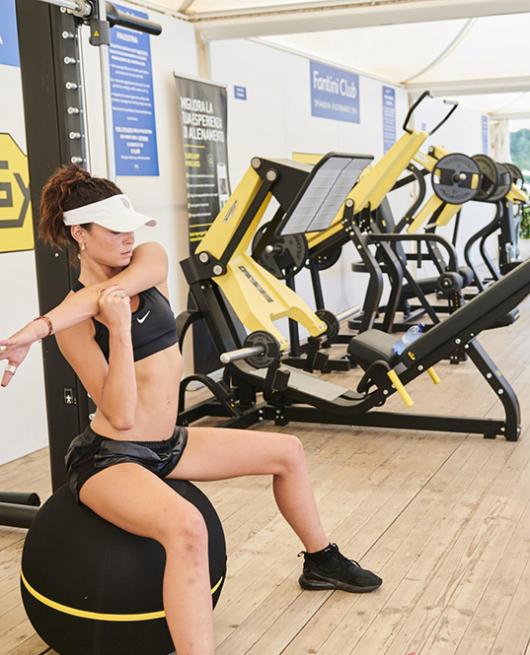 Persone si allenano in palestra con attrezzature moderne su pavimento in legno.