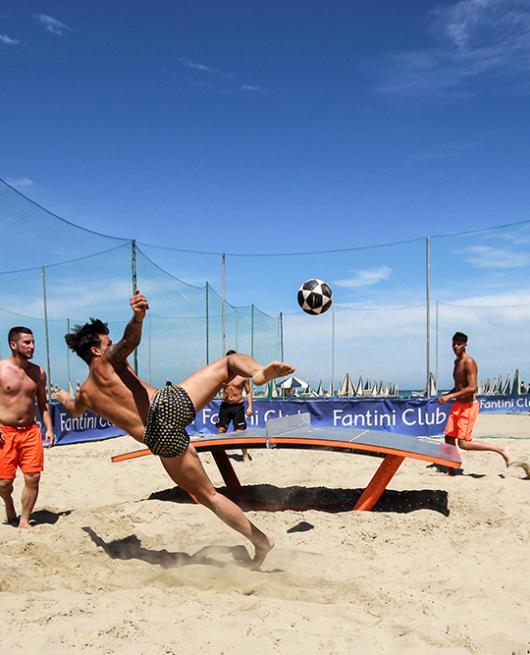 Giocatori giocano a teqball sulla spiaggia al Fantini Club, con reti di protezione.