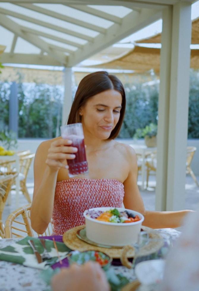 Donna con bicchiere di succo e ciotola di cibo, seduta all'aperto.