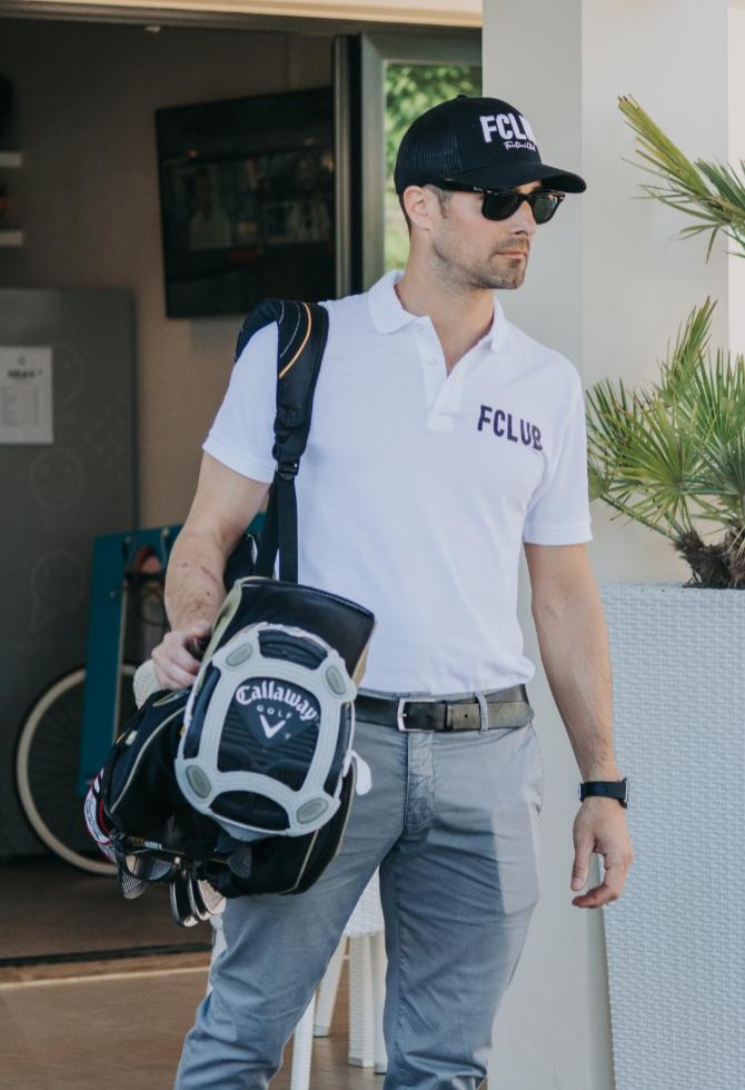 Uomo con cappello e polo FCLUB, trasporta una sacca da golf Callaway.