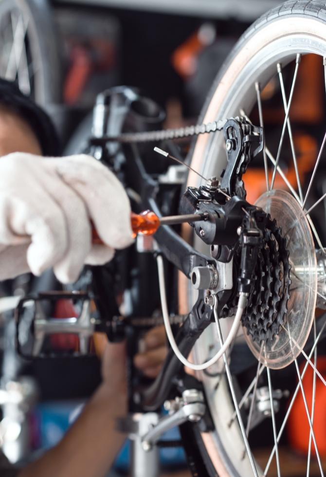 Persona che ripara il deragliatore posteriore di una bicicletta con un cacciavite.