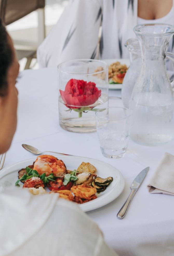 Pranzo elegante con piatto di verdure e pesce, fiore rosso in vaso.