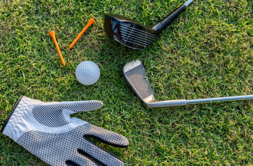 Attrezzatura da golf su erba: mazze, guanti, pallina e tee arancioni.