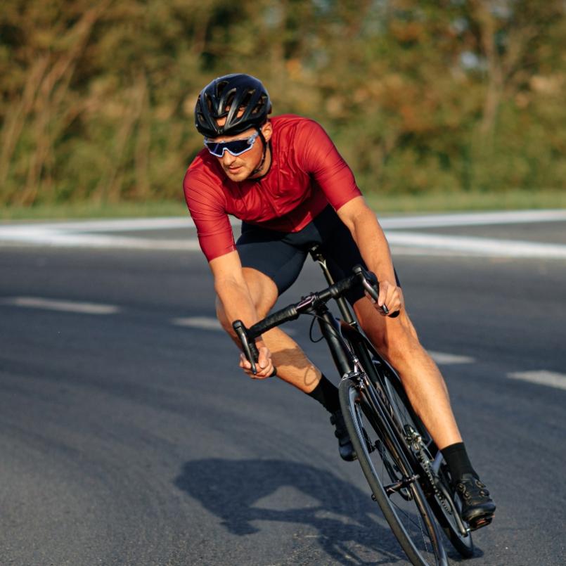 Ciclista in curva su strada, indossa casco e occhiali, maglia rossa.