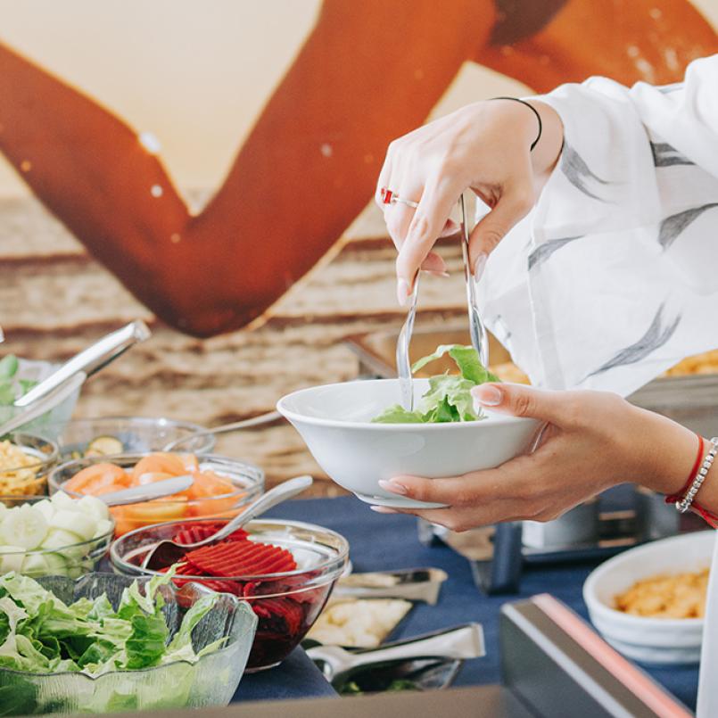 Persona prepara un'insalata al buffet con varie verdure fresche.