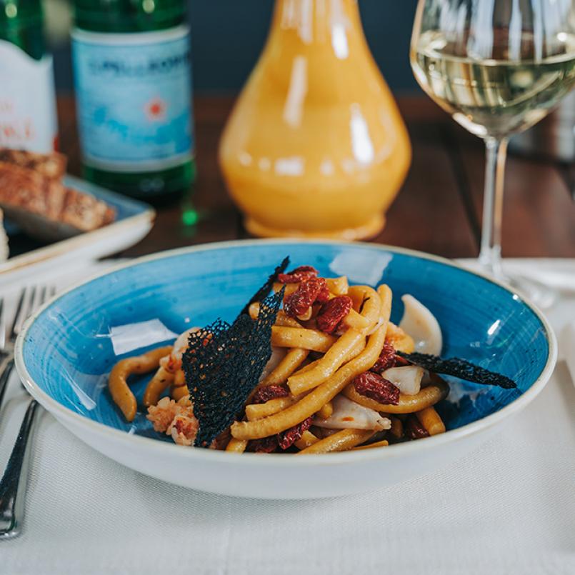 Piatto di pasta con pomodori secchi, pane e bicchiere di vino bianco.